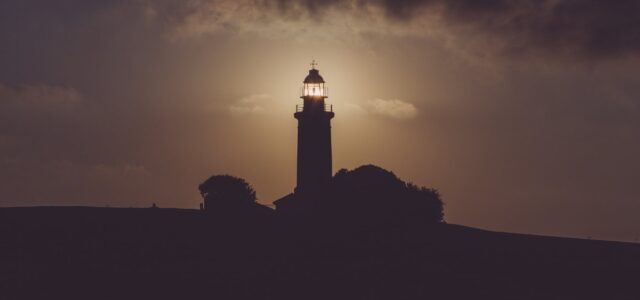 silhouette of light house under gray dark sky
