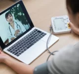 Woman measuring her blood pressure while consulting with doctor via telemedicine at home