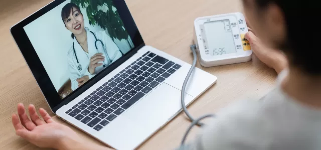 Woman measuring her blood pressure while consulting with doctor via telemedicine at home