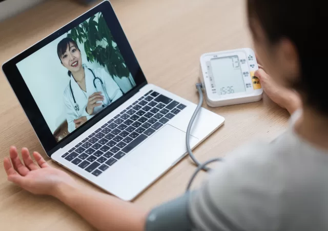 Woman measuring her blood pressure while consulting with doctor via telemedicine at home