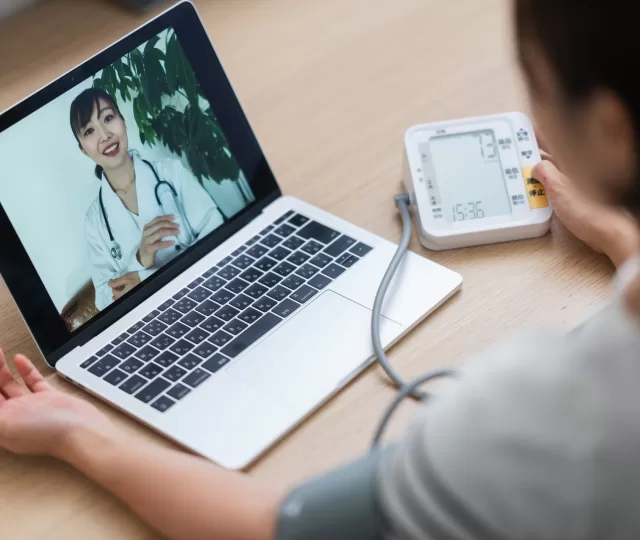 Woman measuring her blood pressure while consulting with doctor via telemedicine at home