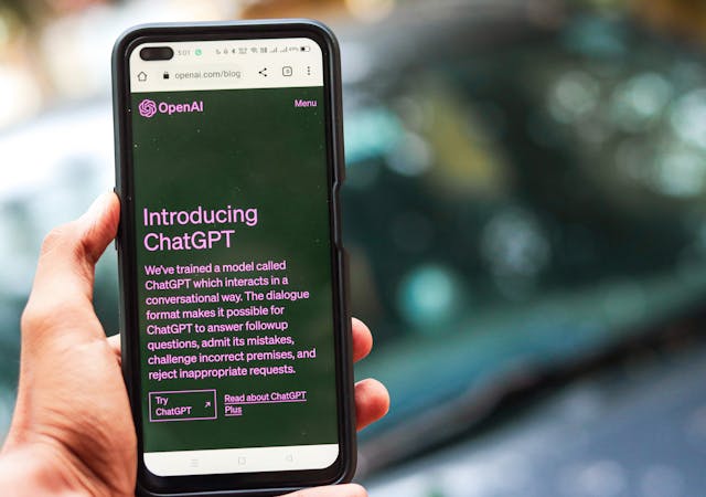 Close-up of a smartphone showing ChatGPT details on the OpenAI website, held by a person.