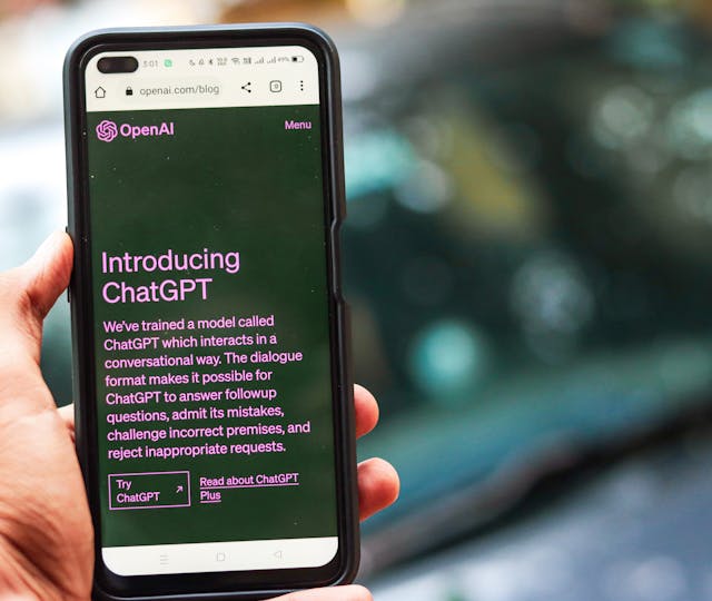 Close-up of a smartphone showing ChatGPT details on the OpenAI website, held by a person.